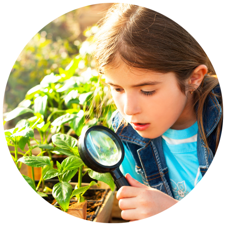 girl looking through magnifying glass at garden plants