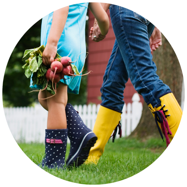 kids in rain boots holding hands and carrying vegetables from the garden