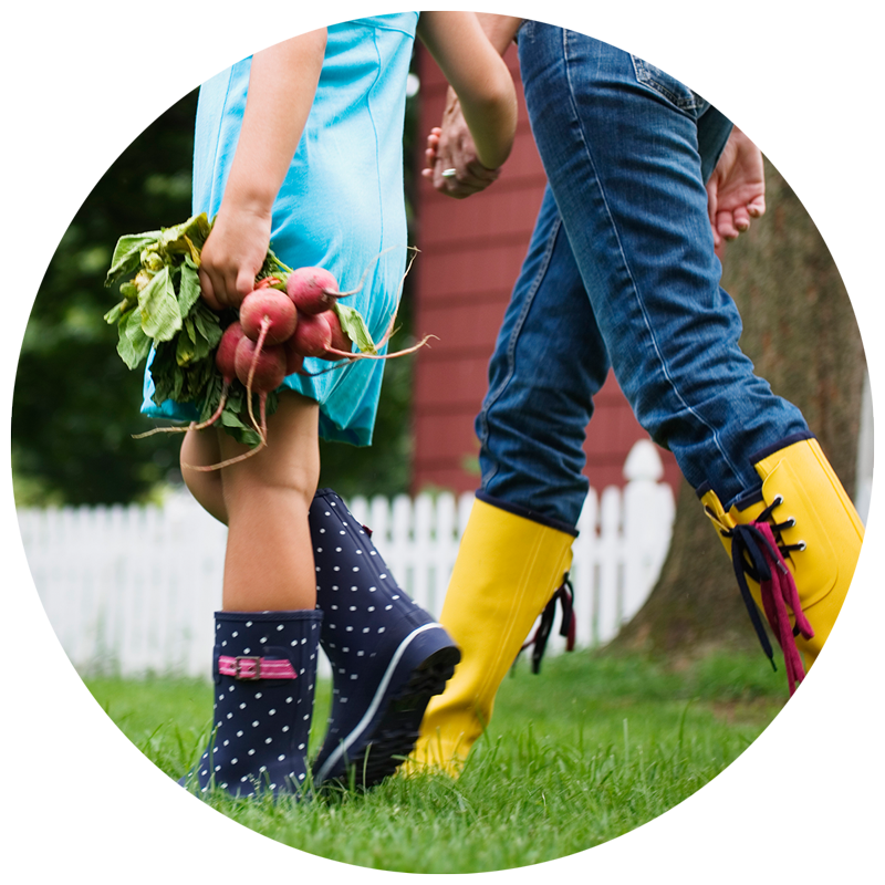 kids in rain boots holding hands and carrying vegetables from the garden