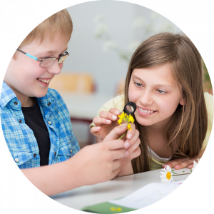 boy and girl in a classroom examining a yellow flower with a magnifying glass