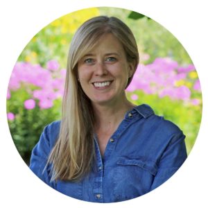 Beth Saunders Beth, a white woman with blond hair, is smiling and wearing a blue shirt in front of garden foliage and pink flowers