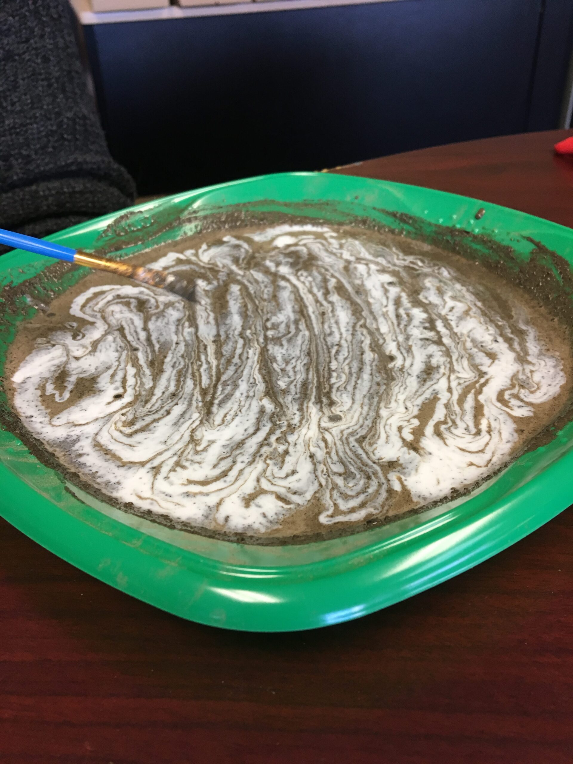 A brush swirling homemade soil paint in a shallow green dish