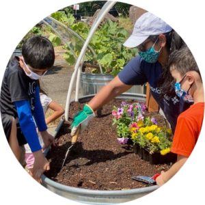 Kids and an adult in face coverings tending a raised garden bed