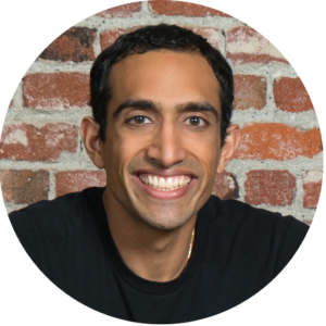 Nikhil Arora copy Nikhil Arora, smiling and wearing a black tshirt, in front of a brick wall