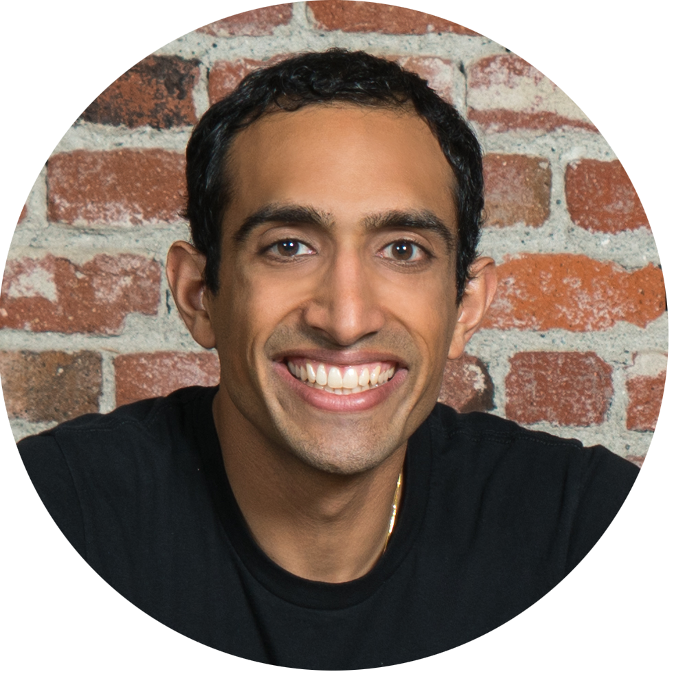 Nikhil Arora, smiling and wearing a black tshirt, in front of a brick wall