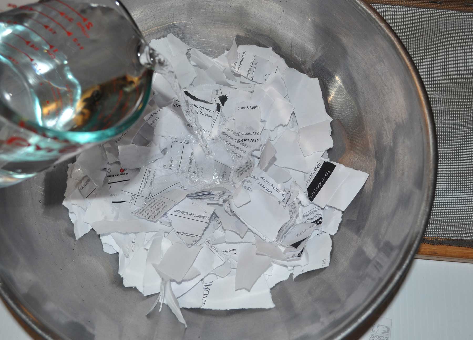 Pouring water over torn scraps of white paper in a bowl