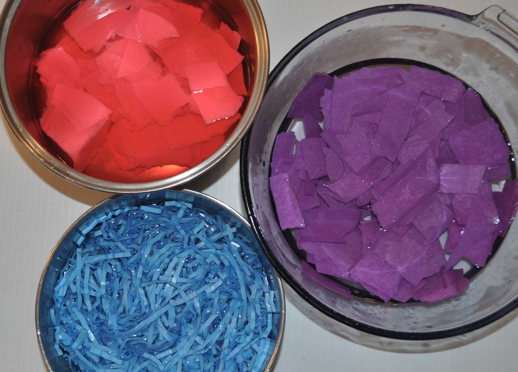 Bowls of torn red, blue and purple paper soaking in water