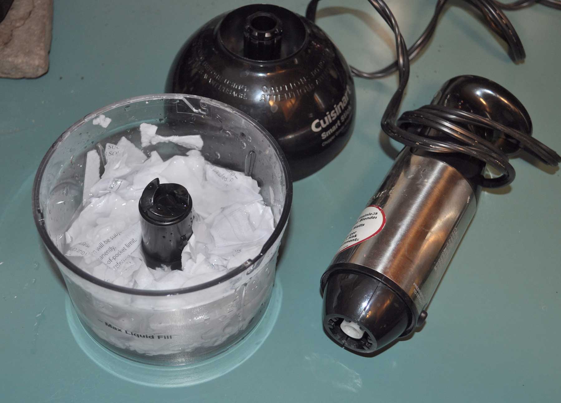A small food processor and an immersion blender next to a container of soaked white paper