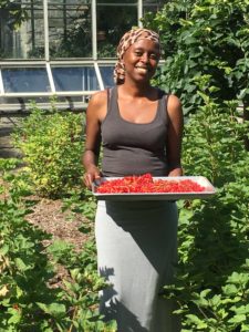 Wambui Ippolito is standing in an urban garden and holding a sheet pan full of bright red berries.