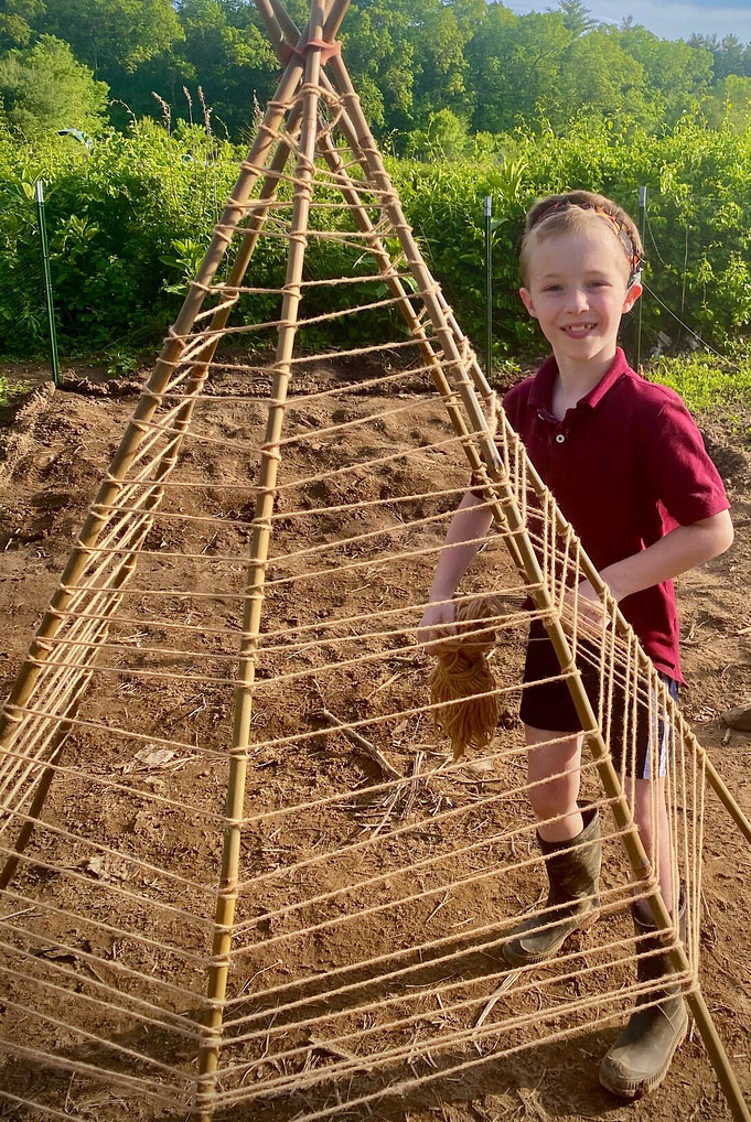 A child standing next to a trellis made of thin wooden sticks and twine
