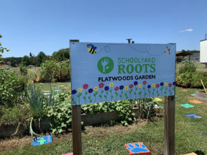 A big white sign in a garden that reads Schoolyard Roots Flatwoods Garden