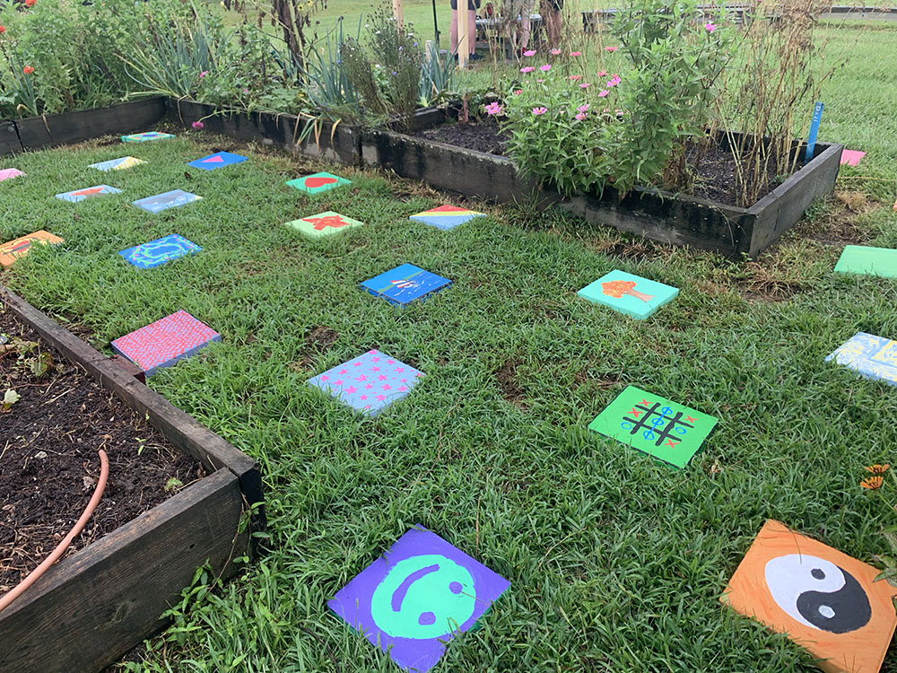 Colorfully painted paving stones on grass, in between raised garden beds.