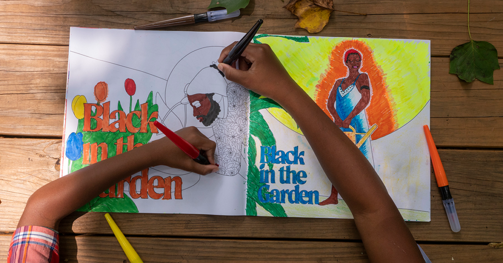 Two Black children's arms are each holding a marker and coloring in a coloring book