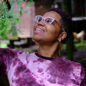 A Black person in a purple tie-dye tshirt tends to a green tree