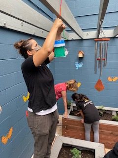 An adult hanging up a structure in a garden space