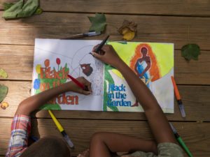 Two Black kids' arms are coloring a brightly colored coloring book.