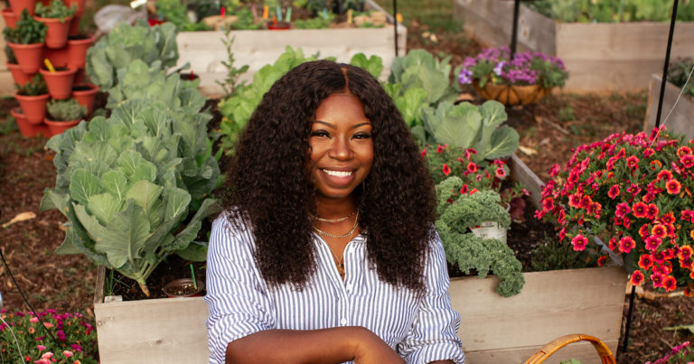 Jasmine smiling and sitting in front of a colorful raised bed garden