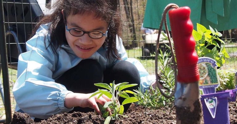 A child wearing glasses reaches out to touch a plant in soil.