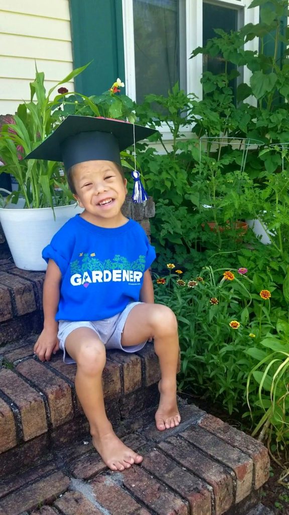A young child in a blue t-shirt, sitting near a garden