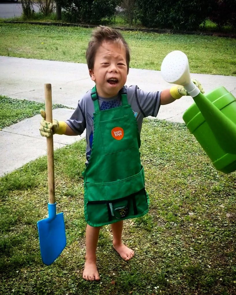 A child holding a big watering can and a child-size shovel