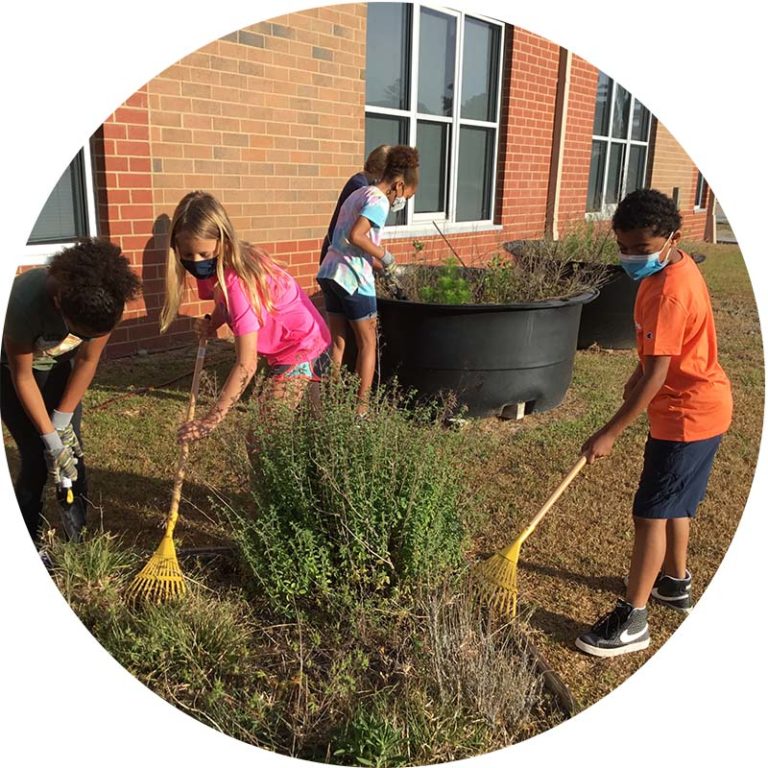 Kids using rakes and other tools to clean out messy garden beds