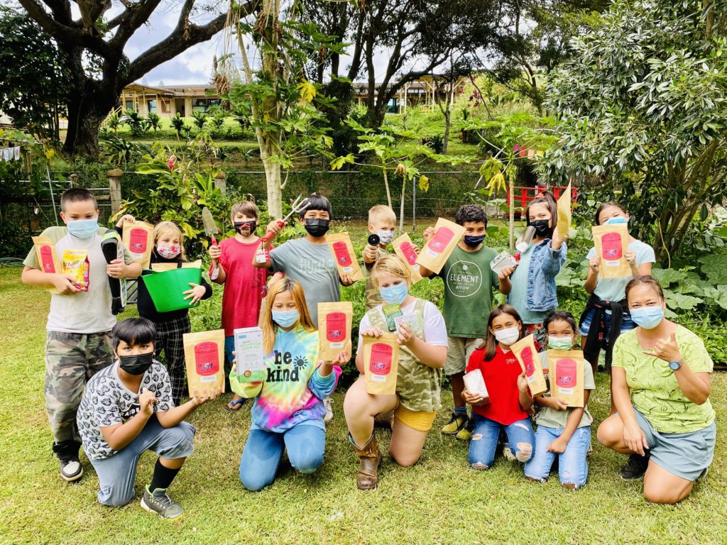 A group of kids outside holding up seed packets and various other things