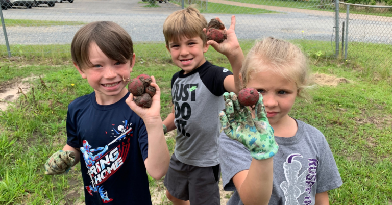 Three kids hold up potatoes for the camera
