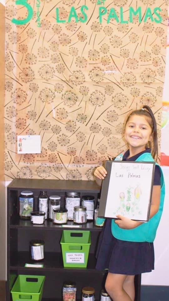 A child in a Girl Scout vest in front of a shelf holding seeds in jars.