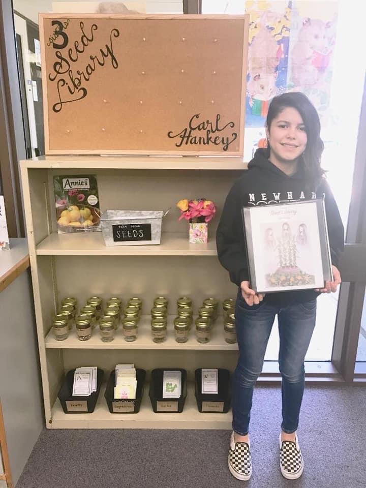 A child holding a folder in front of a big shelf holding seeds in jars.