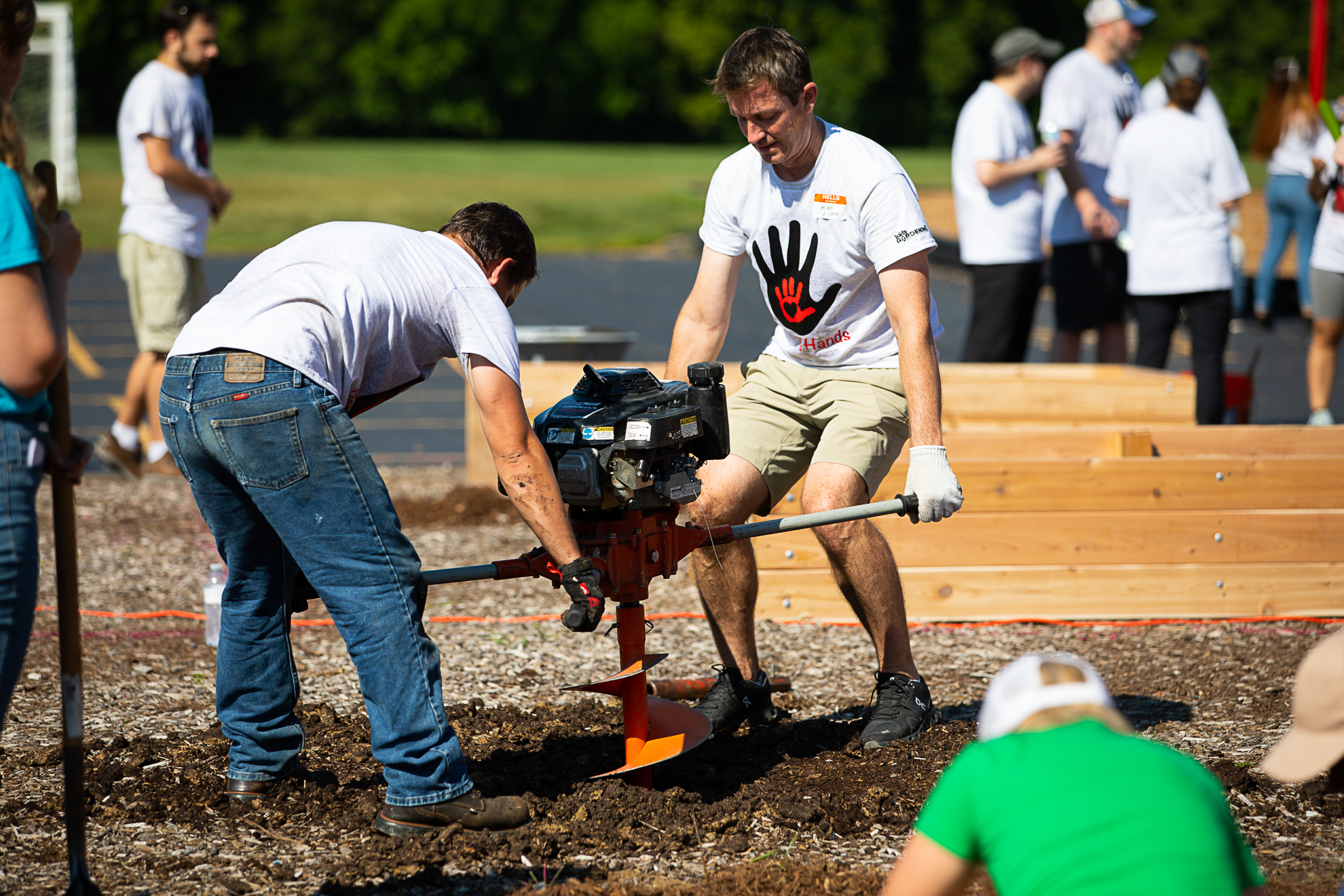 Two people working a gas-powered auger to drill holes