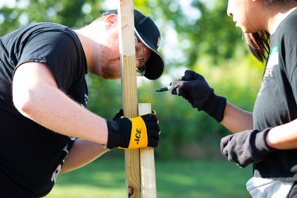 Two people measuring and marking a wooden board