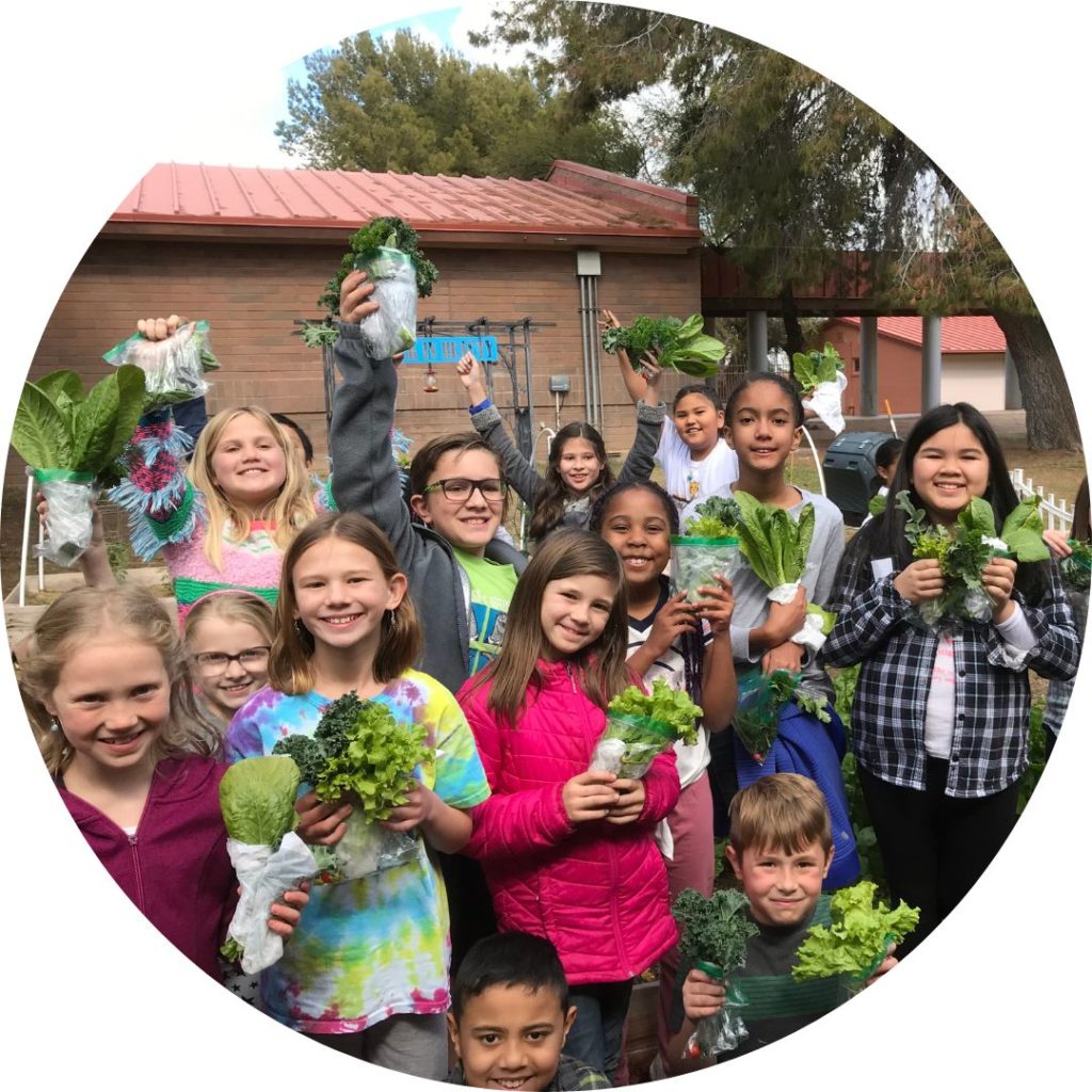 Kids holding up produce outside a school
