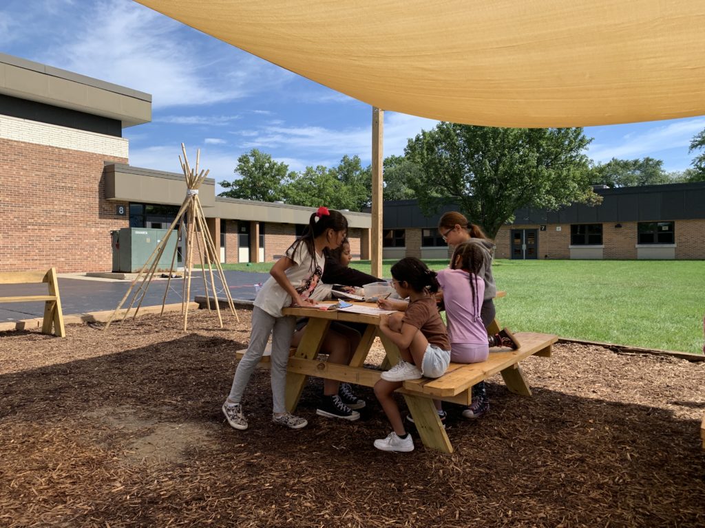 Kids sitting at a picnic table outside under a covering