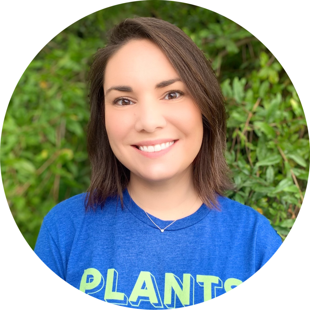 Brunette woman in her mid thirties smiling in front of a leafy background