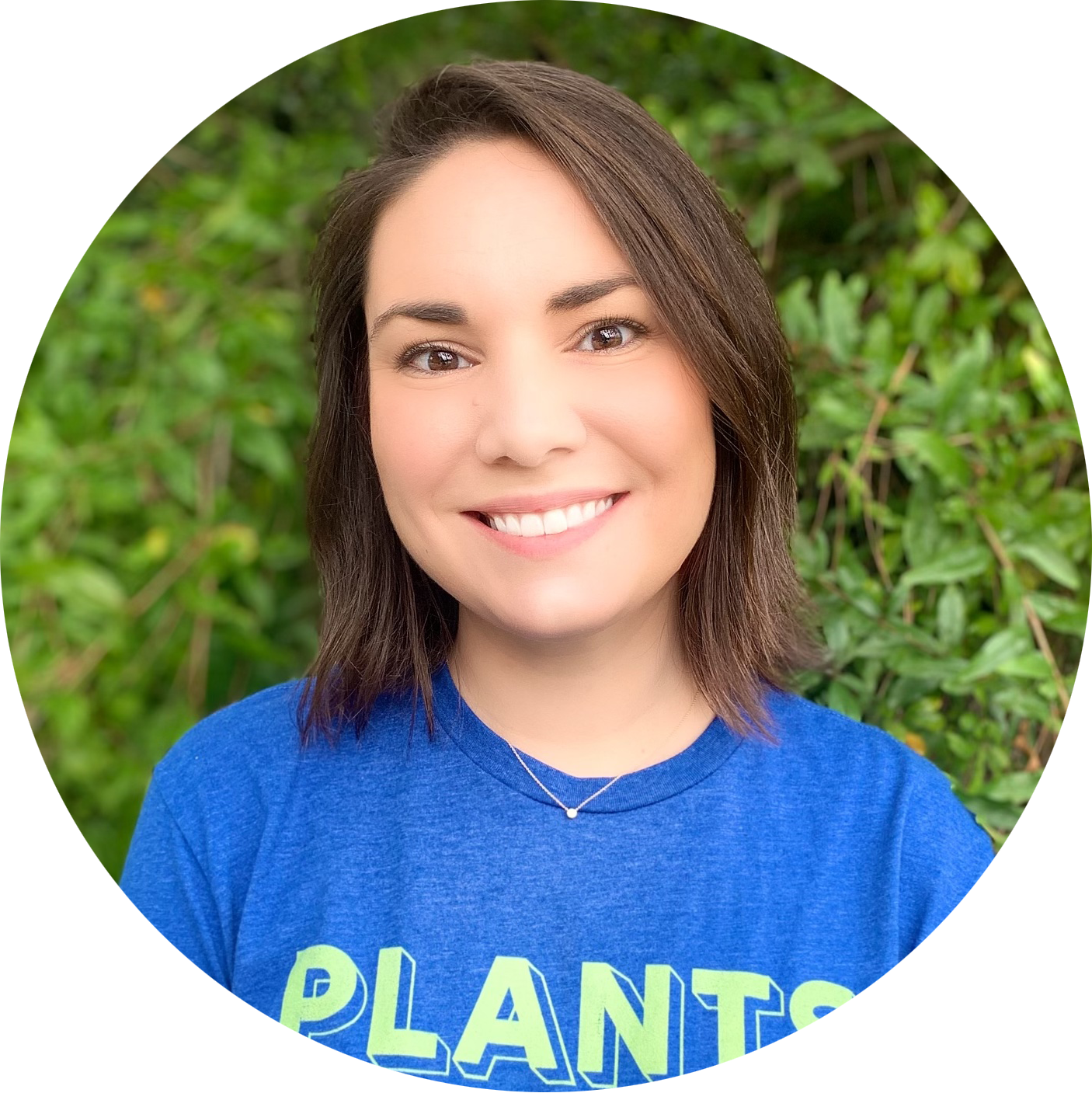 Brunette woman in her mid thirties smiling in front of a leafy background
