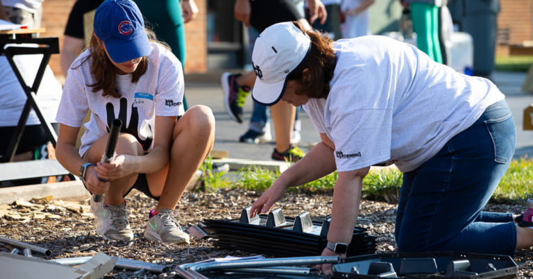 Two people kneeling on the ground, putting something together