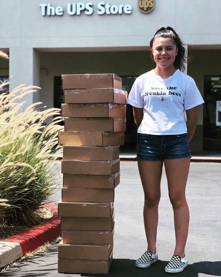 A teen standing next to a tall stack of boxes in front of a UPS Store