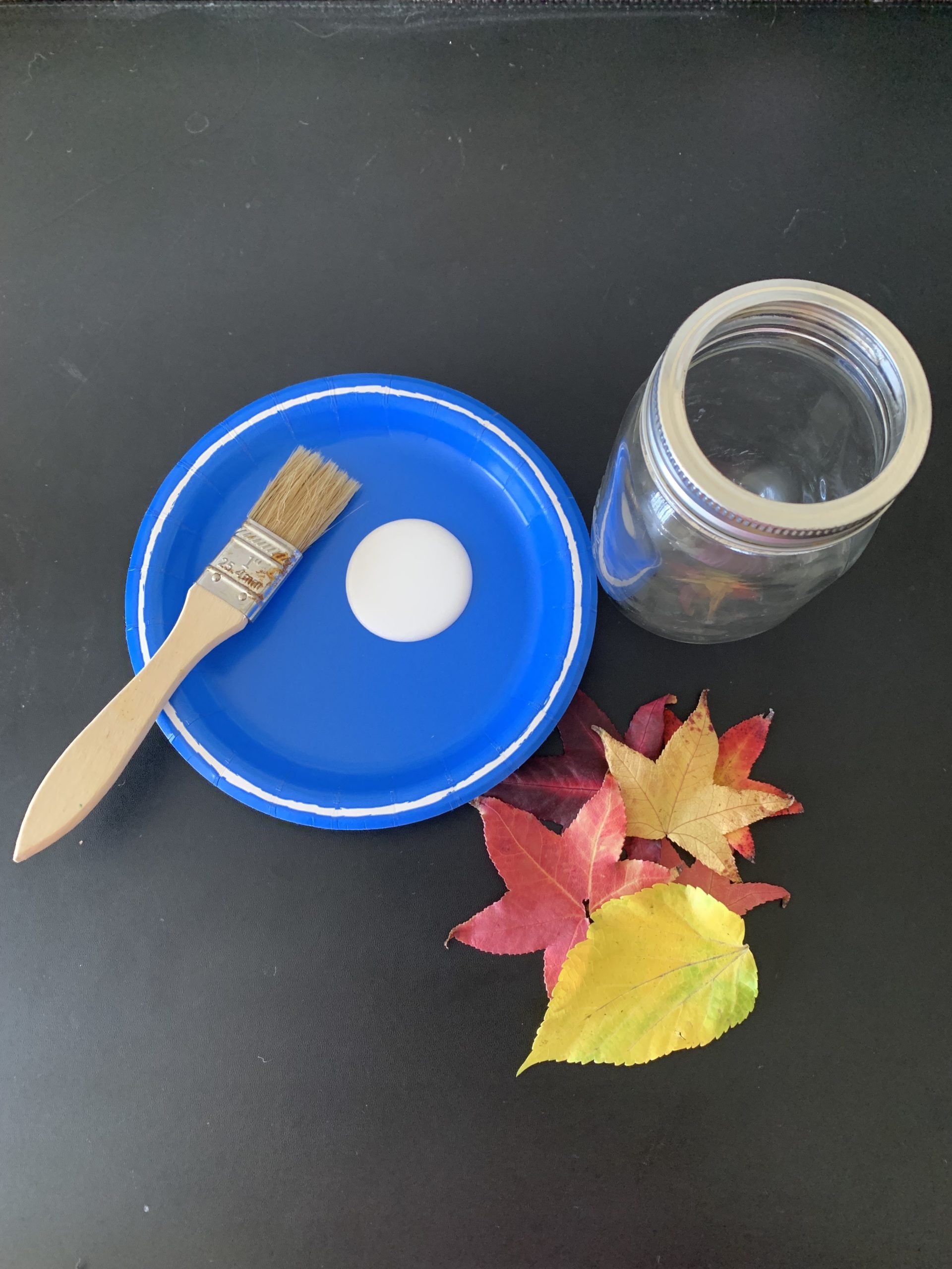 A dab of glue on a blue plate, next to a jar and leaves