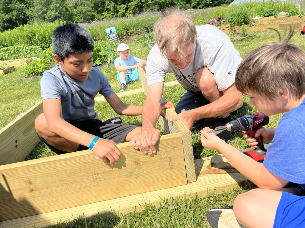 An adult and two kids work together to build a raised bed.