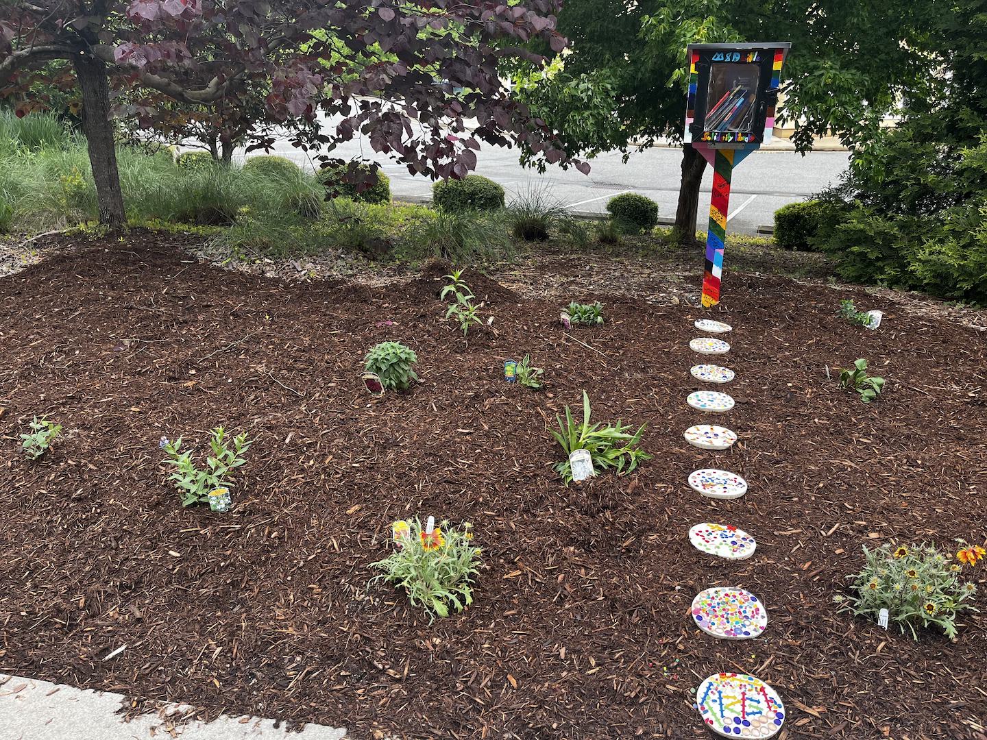 Stepping stones in a garden leading to a Pride-themed "little free library" structure