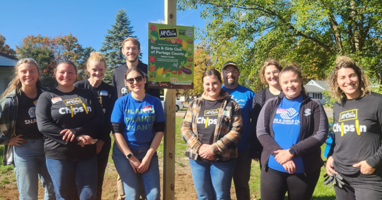 Smiling adults are standing around a sign in a garden.
