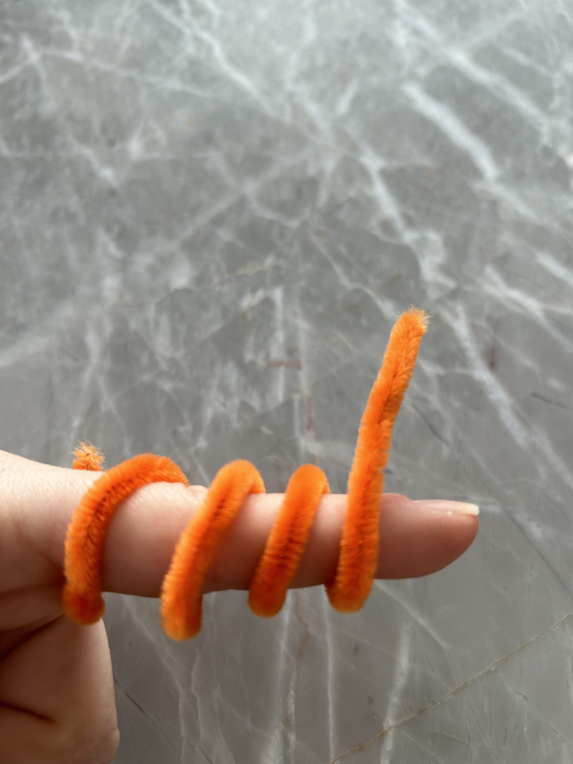 An orange pipecleaner curled around a finger.