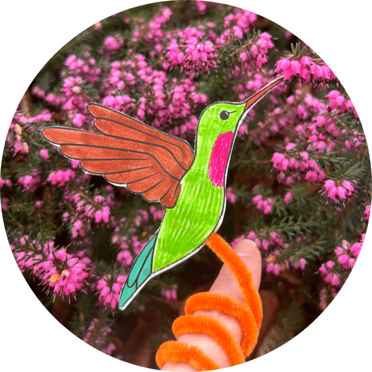 A paper hummingbird on a pipecleaner, which is twirled around a person's finger.