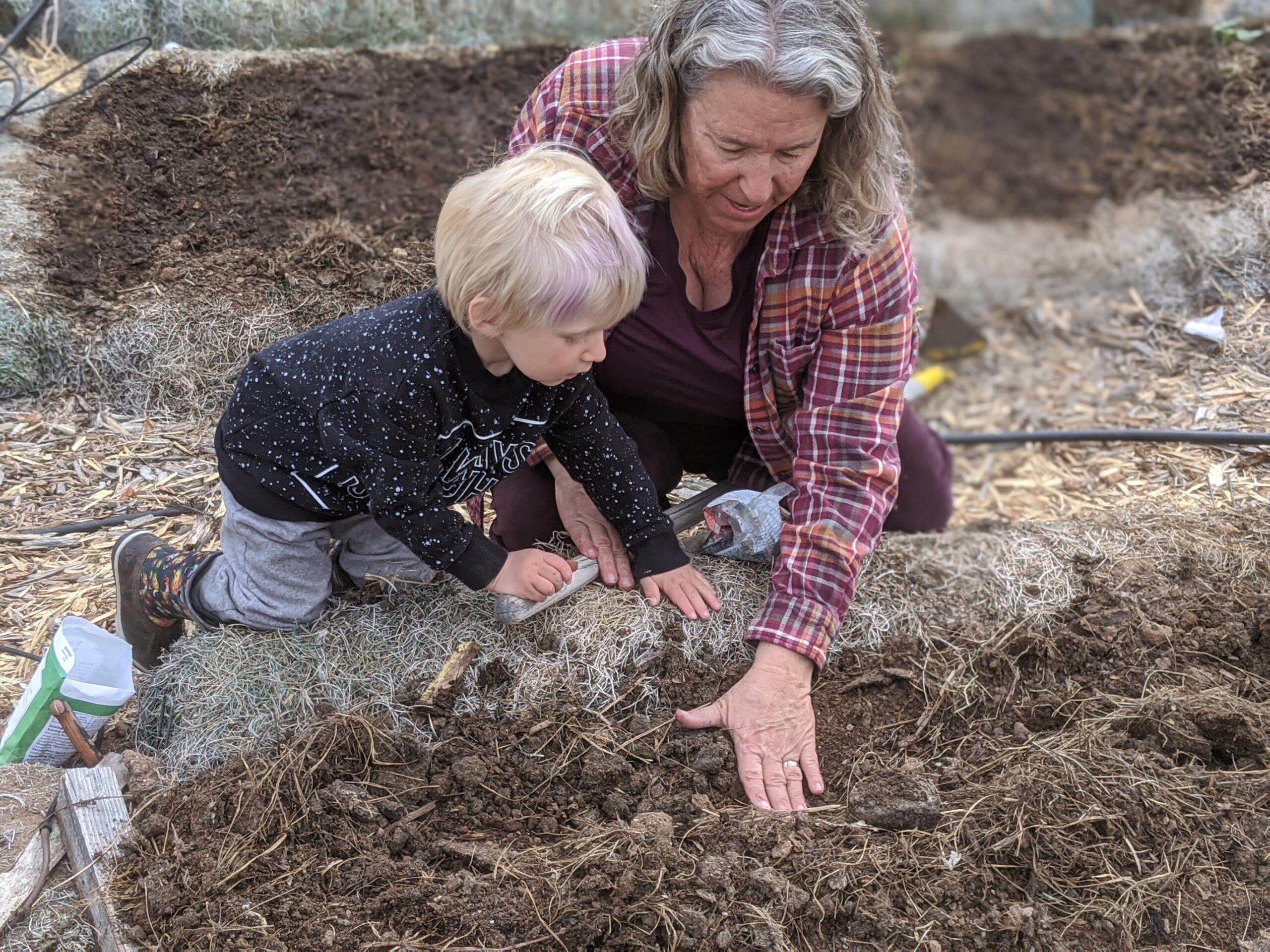 An adult and child work together to plant seeds in soil.