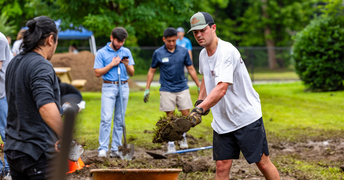 A person in shorts and a t-shirt is shoveling soil into a wheelbarrow.