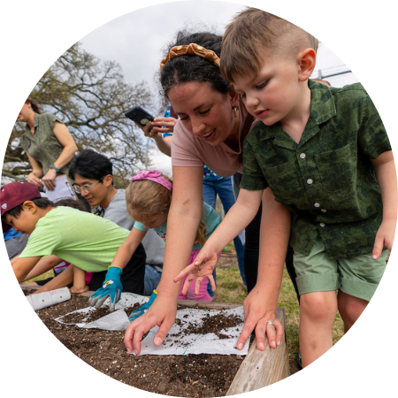 An adult and a child looking at a paper together outside in a garden bed.