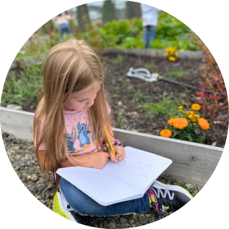 A child outside in the garden holding a notebook in their lap