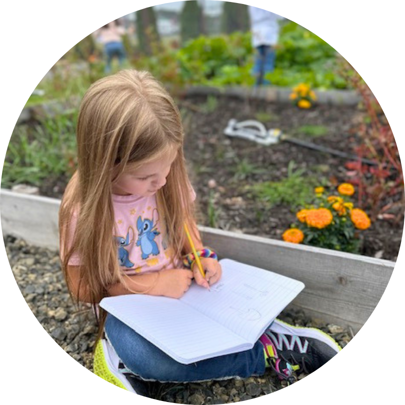 A child outside in the garden holding a notebook in their lap
