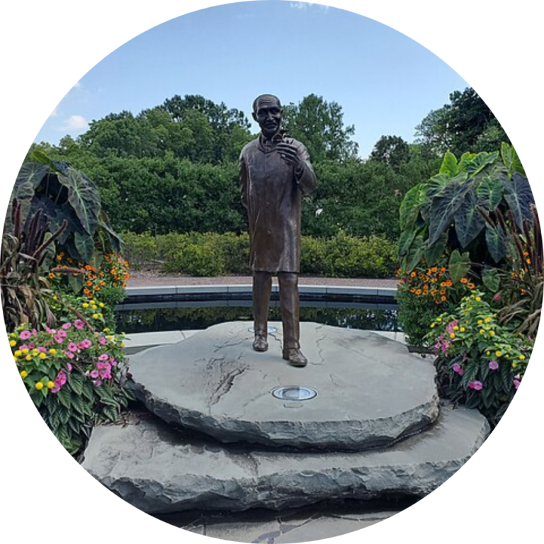 A statue of a person on a rock in a manicured garden space.