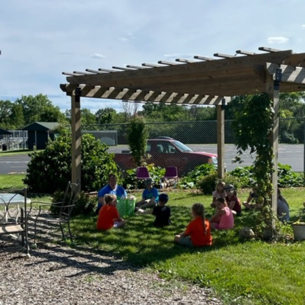 A wooden pergola that is providing shade to the children sitting underneath.